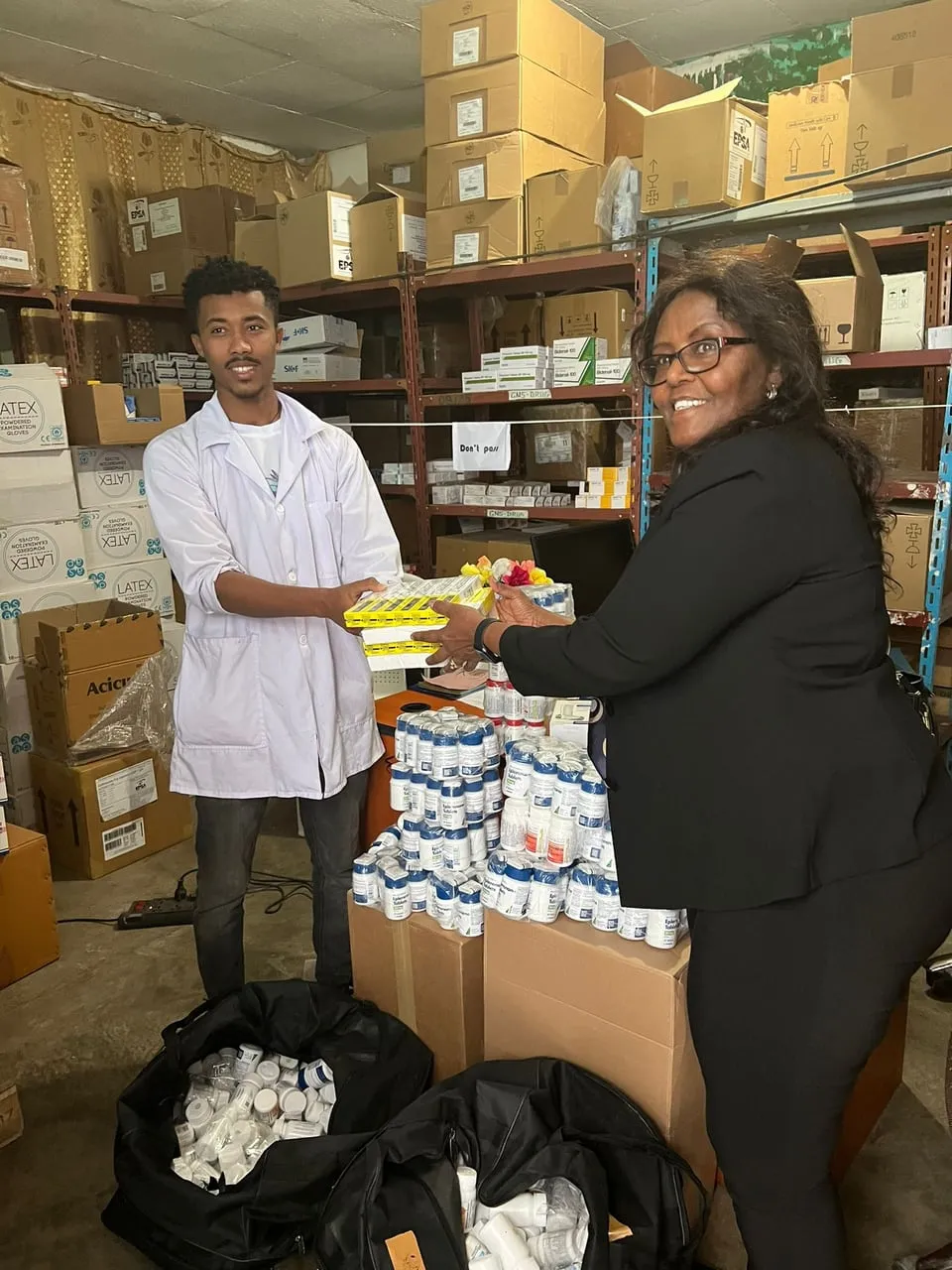 Two adults hold boxed supplies in a room with stocked shelves
